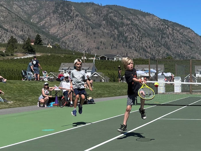 Kids jump in the air as they hit tennis balls on the court. It is a beautiful day. Washington state youth tennis. Youth tennis camps and lessons.