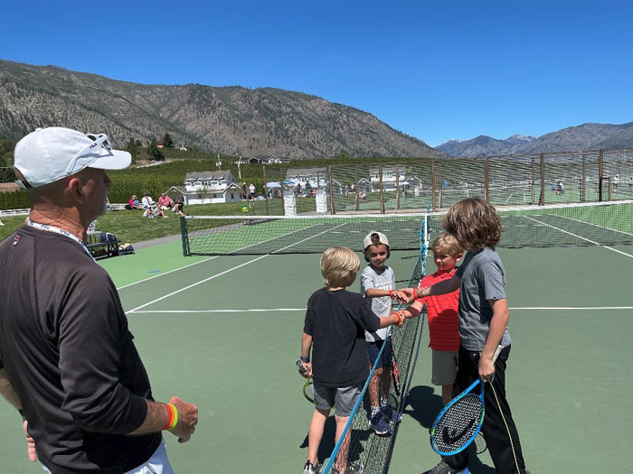 Four youth tennis players hit high-fives as a coach looks on. Kids tennis lessons and camps in Washington State.