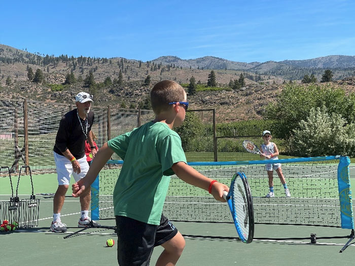 A young child wearing a green shirt hits a tennis ball in a youth tennis lesson. Kids tennis.