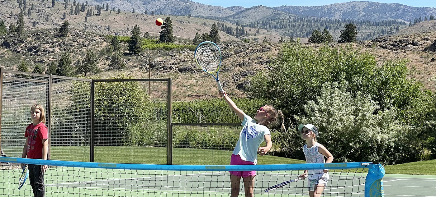 A child jumps up to hit a tennis ball over the net. Washington state tennis and youth tennis camps.